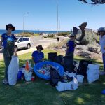 Smiling volunteers standing behind rubbish collected from beach clean up